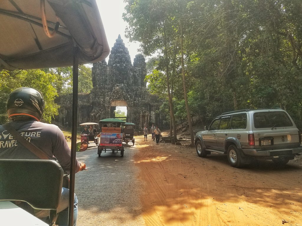 Tuk tuks driving through an ancient gate at the Angkor Temples complex