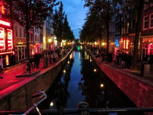 Tourists walking along a canal in the evening in Amsterdam's famous most famous attraction, the Red Light District