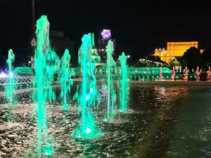 Piata Unirii Fountain at night with green lights illuminating the water and the Palace of the Parliament glowing in the background