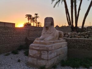 Individual statue of the Avenue of Sphinxes with the sun setting behind